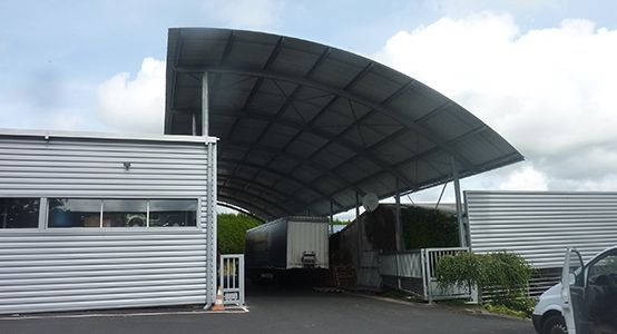 Entrée d'entrepôt avec un toit métallique incurvé et un camion stationné à l'intérieur.