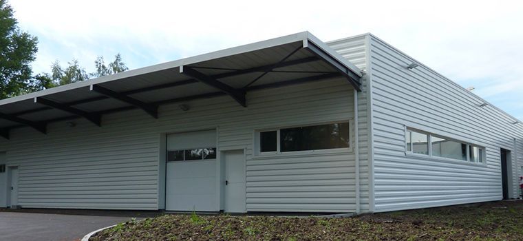 Un bâtiment industriel en métal blanc avec un auvent. Le bâtiment possède une porte de garage et des fenêtres.