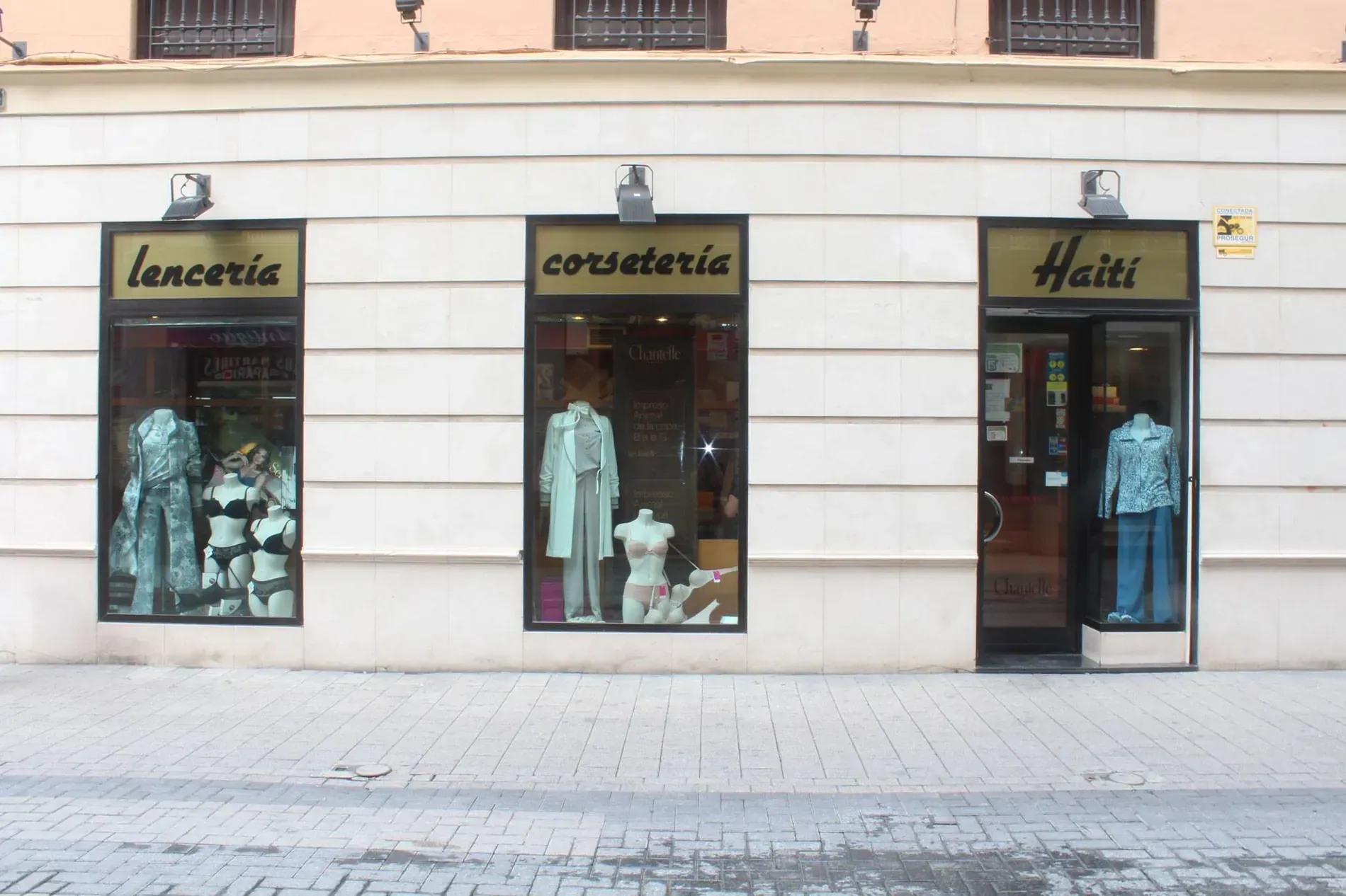 Tiendas: lencería, corsetería, Haití, con escaparates de ropa. Fachada de edificio beige, acera.