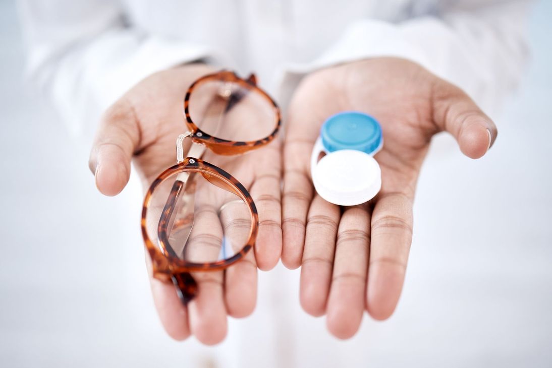 Une personne tenant dans ses mains des lunettes de vue et des lentilles de contact.