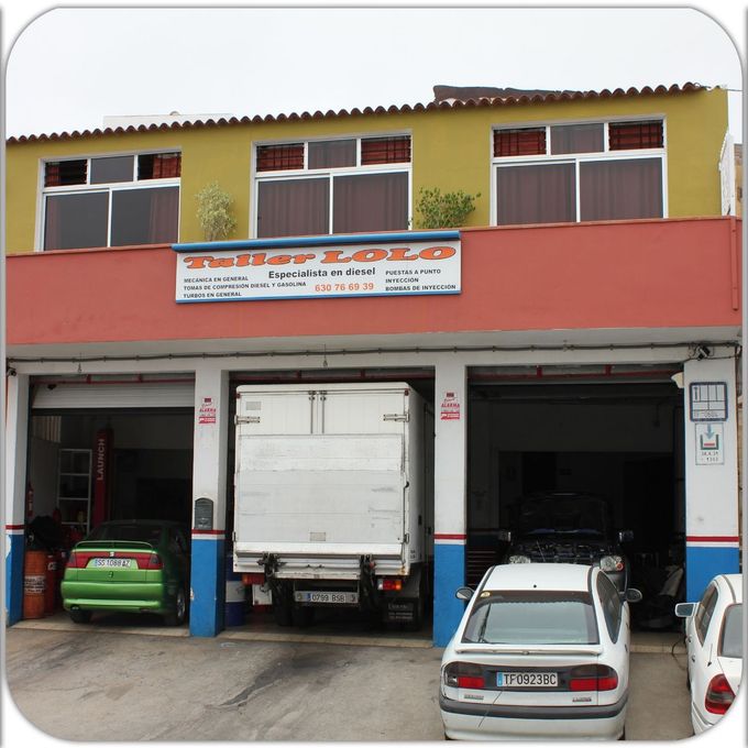 Taller mecánico con camiones y coches aparcados en los boxes abiertos del garaje.