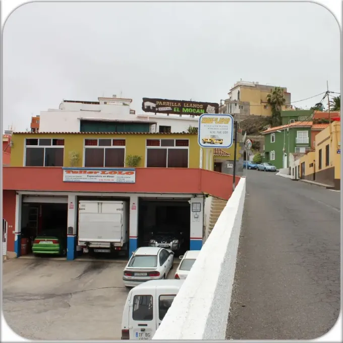 Escena callejera con un edificio amarillo y rojo junto a una carretera empinada cuesta arriba y vehículos estacionados.
