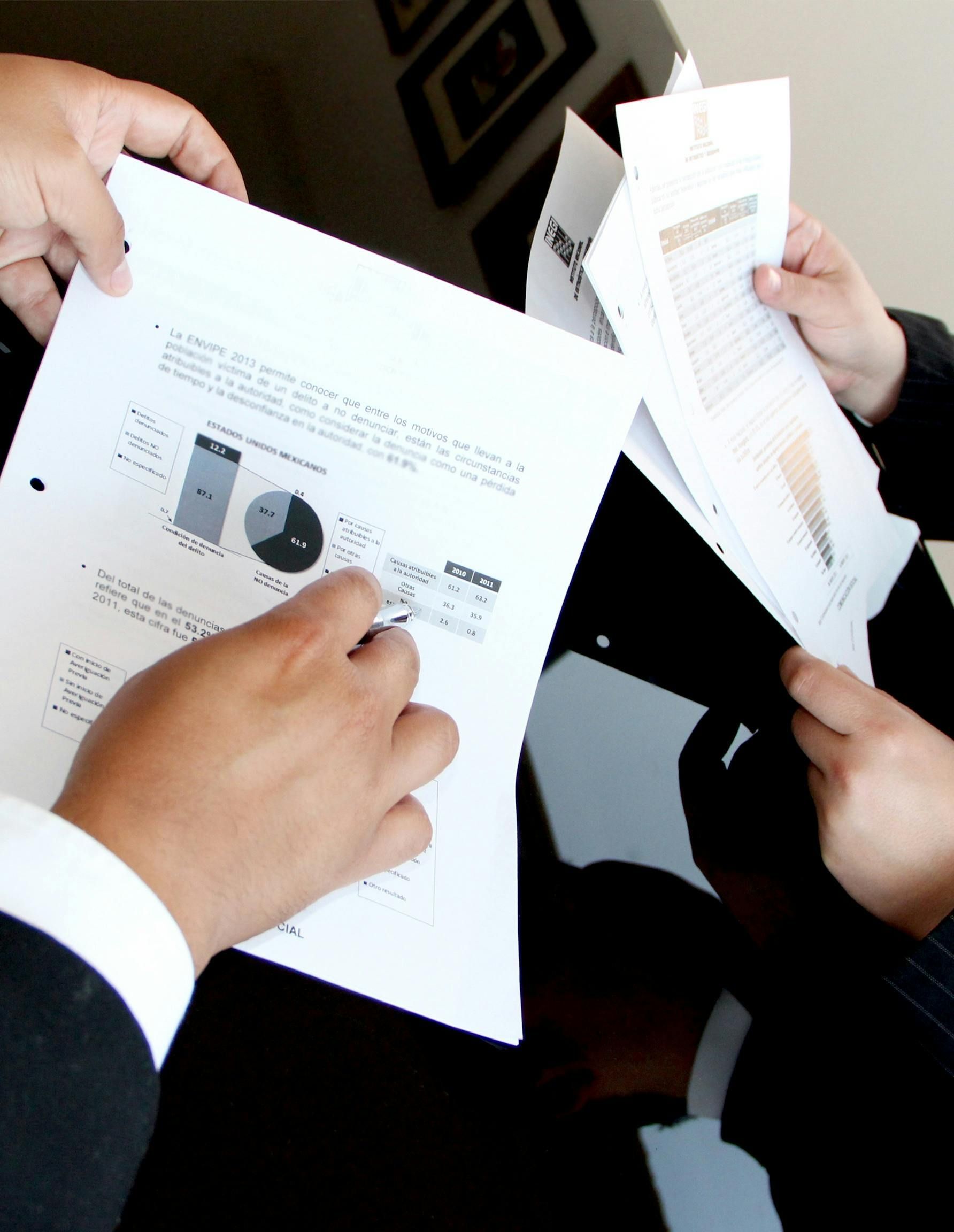 Manos revisando gráficos y documentos impresos en una reunión de negocios.