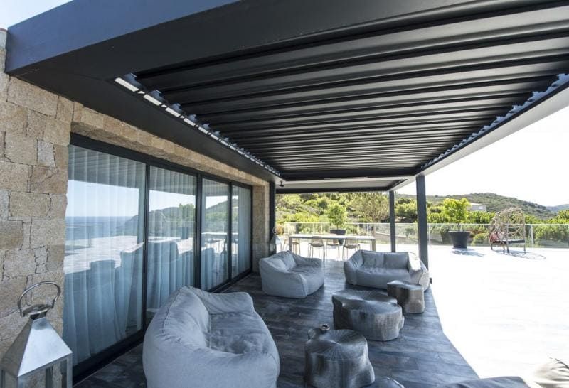 Coin terasse avec fauteuils sous une grande pergola.