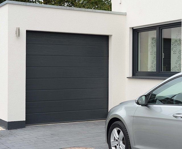 Un véhicule gris devant une porte de garage noir anthracite.