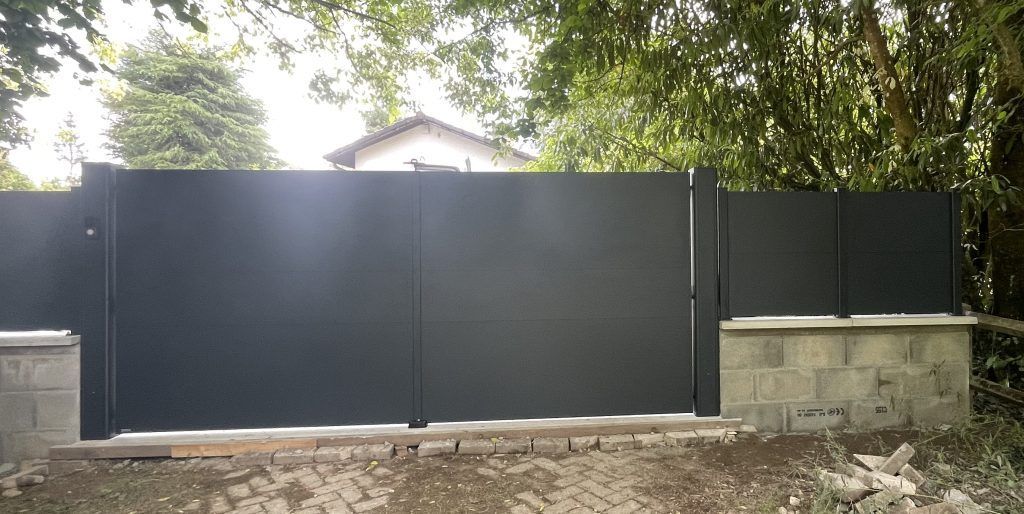 Un portail noir fermé sous un arbre.