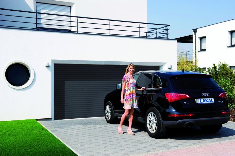 Une femme à côté d'un véhicule noir  devant une porte de garage.