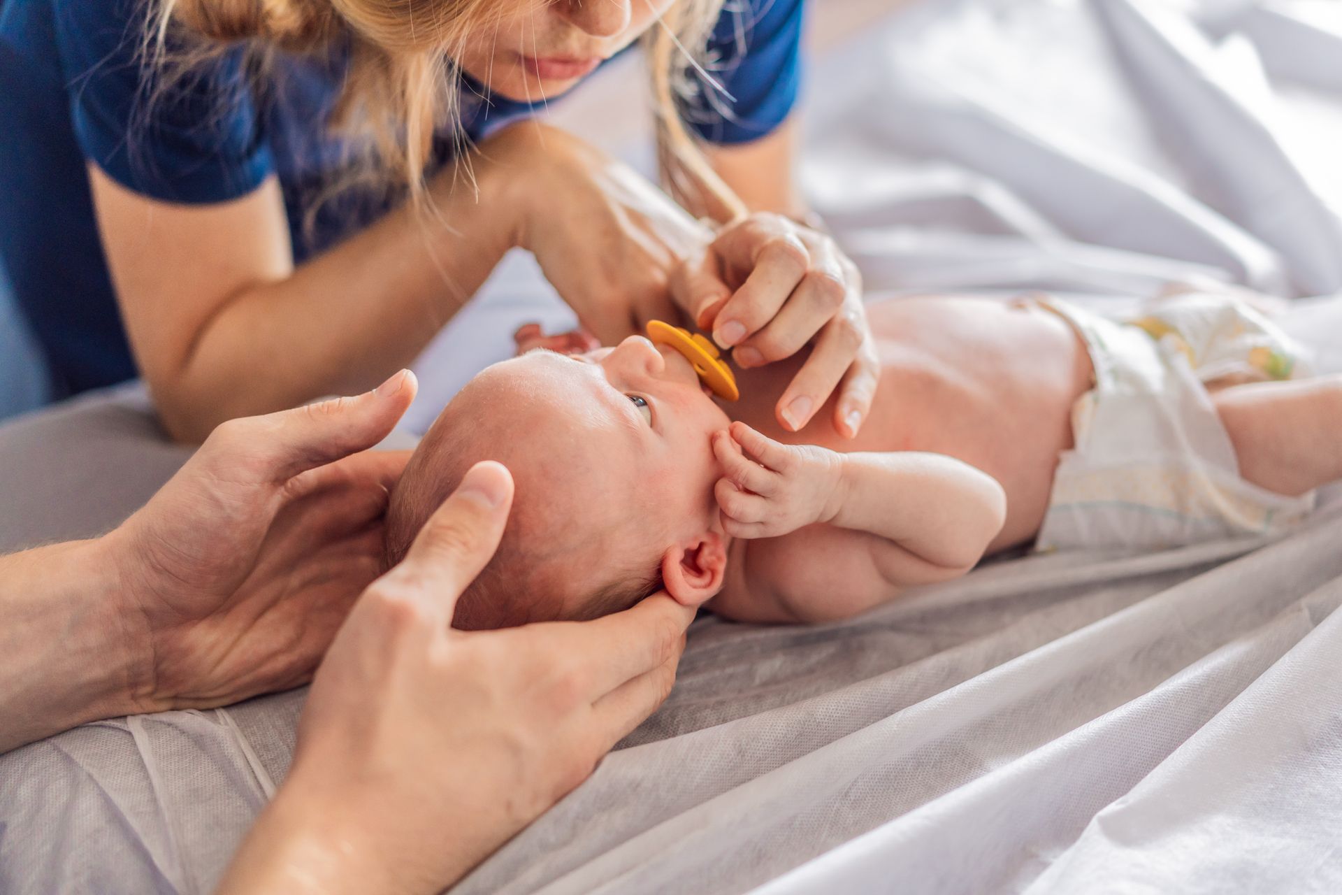 Personne réconfortant un nourrisson sur son lit, lui offrant une tétine, les mains soutenant sa tête.