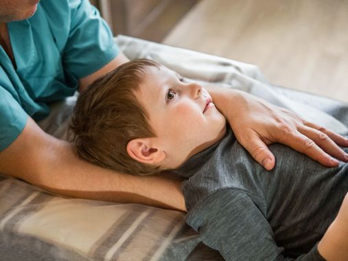 Un enfant allongé reçoit un massage. Les mains d'un adulte sont posées sur sa poitrine et son dos.