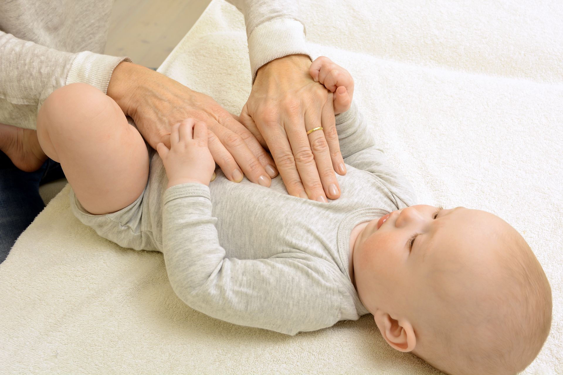 Des mains massent doucement la poitrine d'un bébé allongé sur une surface blanche, probablement à des fins thérapeutiques.