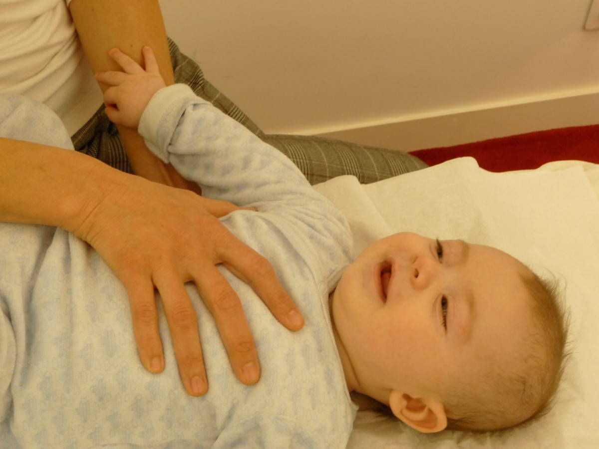 Un bébé allongé sur une surface blanche, tenu et touché par les mains d'une personne.