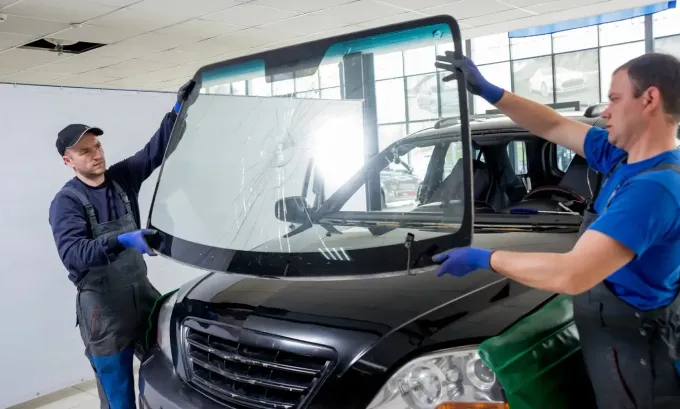 Dos trabajadores instalando un parabrisas en un coche negro en un garaje.