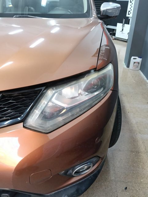 Persona puliendo un coche negro con una pulidora rotativa en un garaje bien iluminado.
