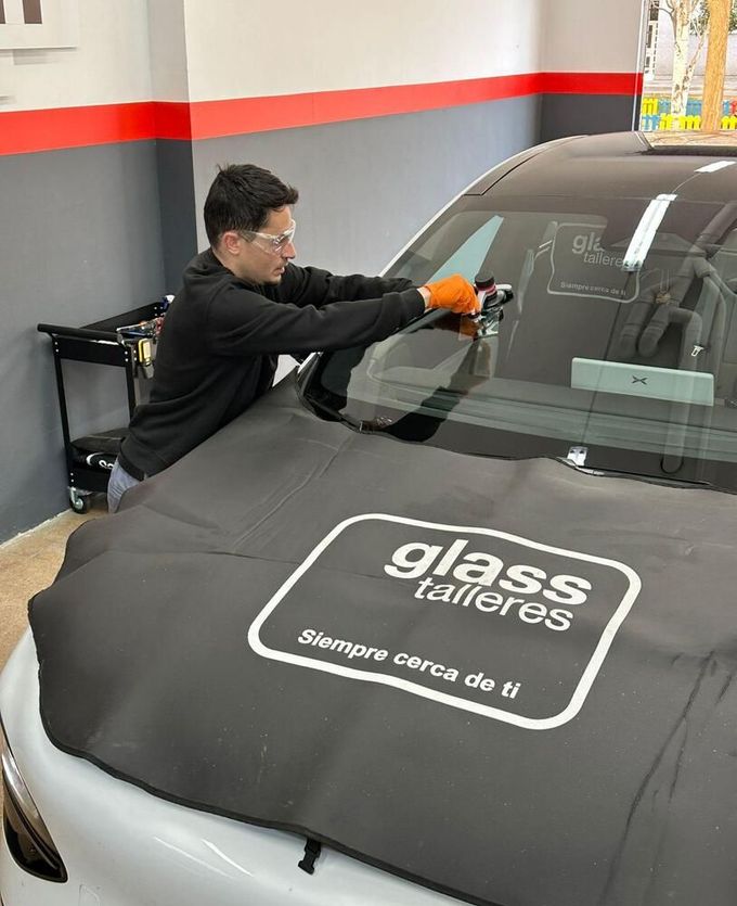 Persona con guantes que utiliza una herramienta de reparación de parabrisas en el parabrisas de un automóvil en un garaje.