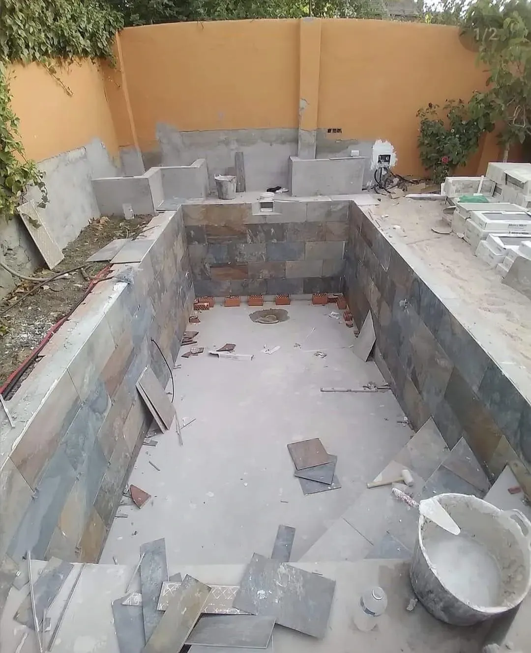 Piscina en construcción, paredes revestidas de piedra, base de hormigón, ubicada al aire libre.