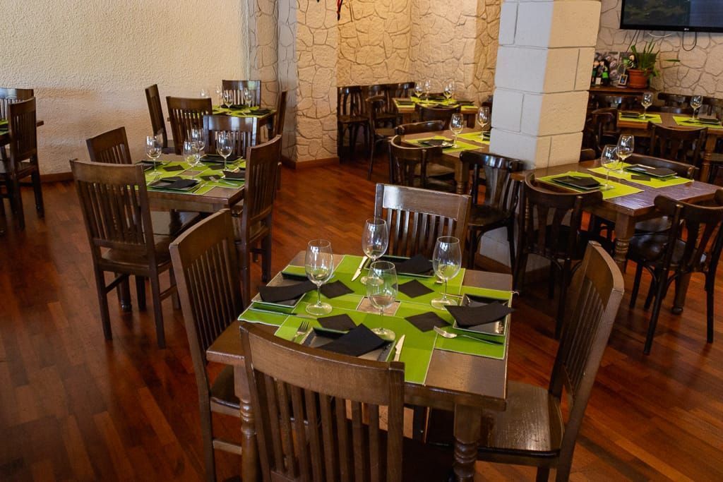 Interior de restaurante con mesas y sillas de madera y suelo oscuro. Mesas preparadas para comer.