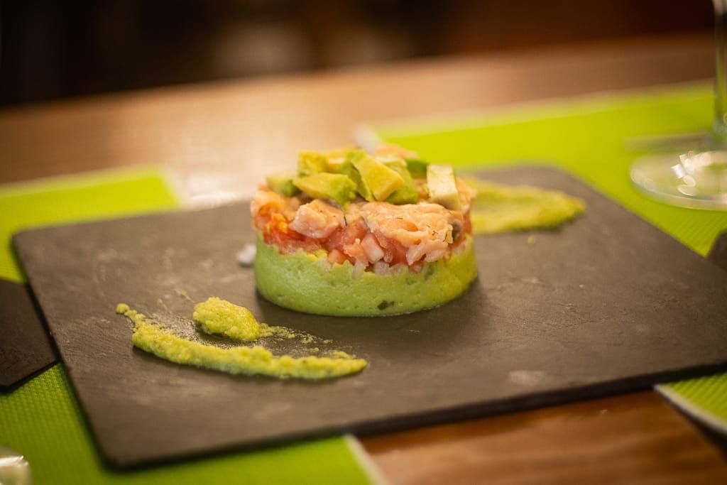 Torre de salmón y aguacate sobre plato de pizarra con salsa verde, ambientación de restaurante.
