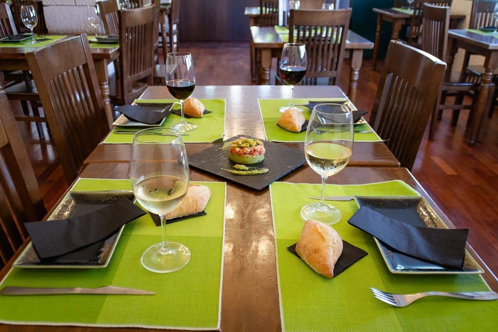 Juego de mesa de restaurante para cenar: manteles individuales verdes, copas de vino, panecillos y aperitivo sobre una mesa de madera oscura.