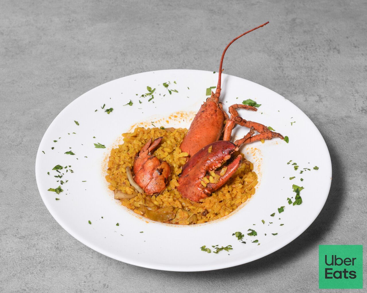 Paella de langosta y camarones en plato blanco con guarnición de perejil.