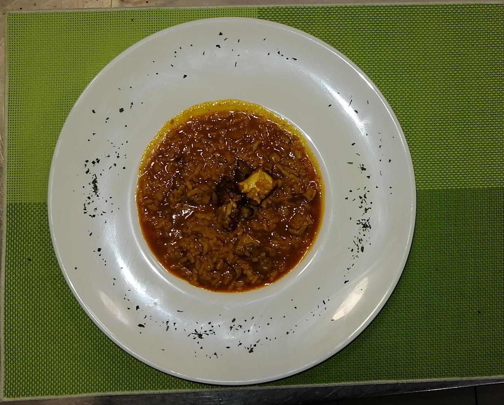 Sopa en un recipiente blanco con guarnición negra sobre una estera verde.