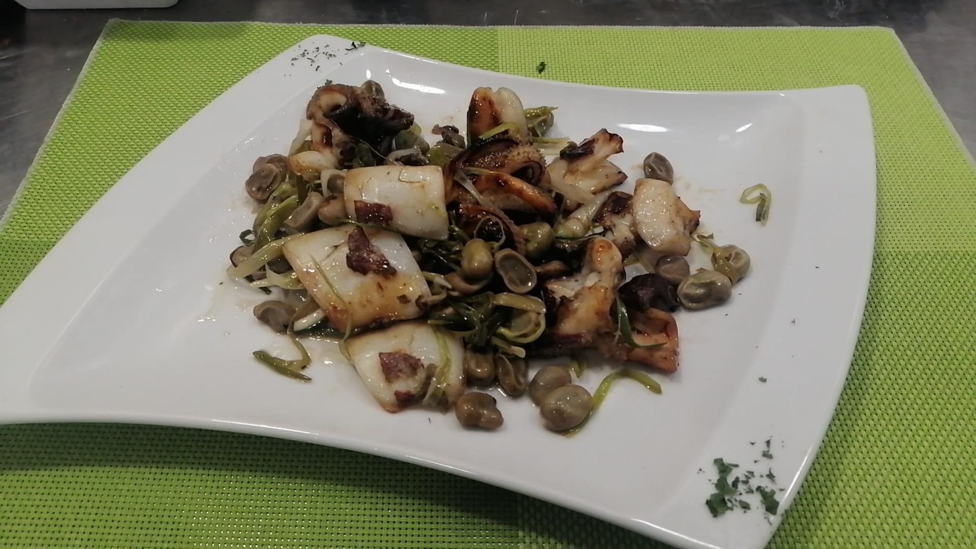 Plato de mariscos a la parrilla con verduras verdes en un plato blanco.