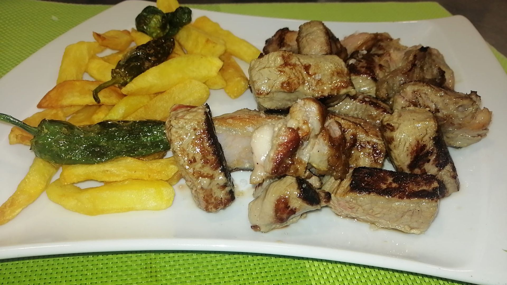 Plato con patatas fritas, trozos de carne a la parrilla y pimientos verdes fritos.