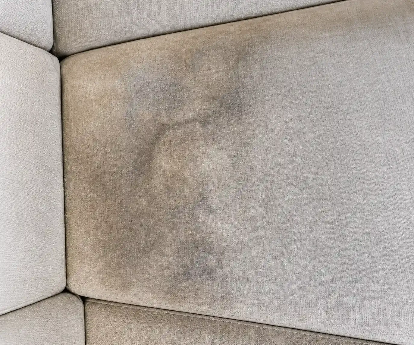 Esquinero de sofá tapizado en color beige con una mancha oscura en el cojín del asiento.