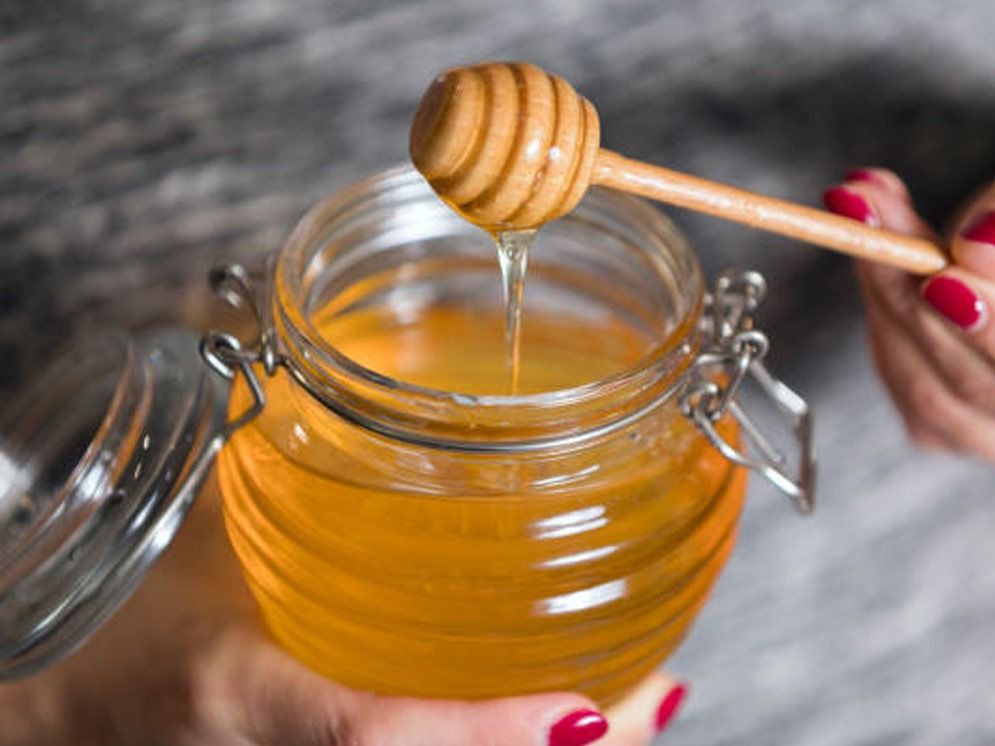 Una mujer sostiene un tarro de miel con un cucharón de miel que sobresale de él.