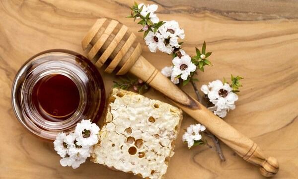 Un cucharón de miel de madera, un panal y flores sobre una mesa de madera.