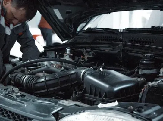 Mecánico inspeccionando el motor de un coche bajo el capó abierto en un garaje.
