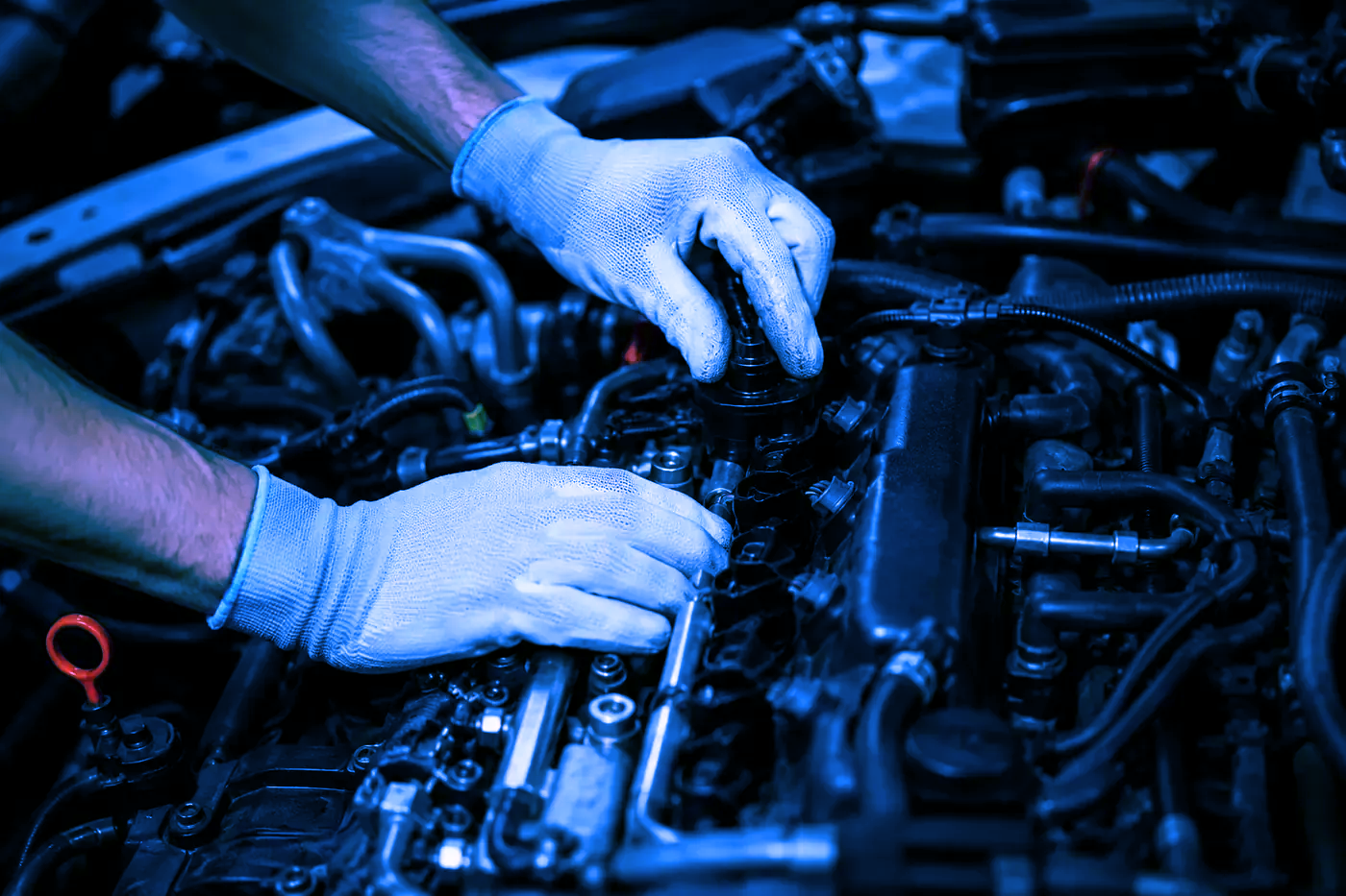 Manos enguantadas trabajando en el motor de un coche bajo luz azul.