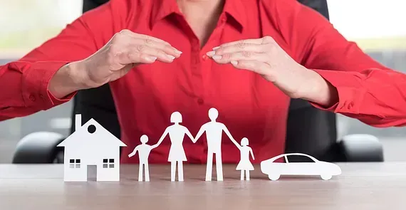 Una mujer está sentada en una mesa con un recorte de papel de una familia, una casa y un automóvil.