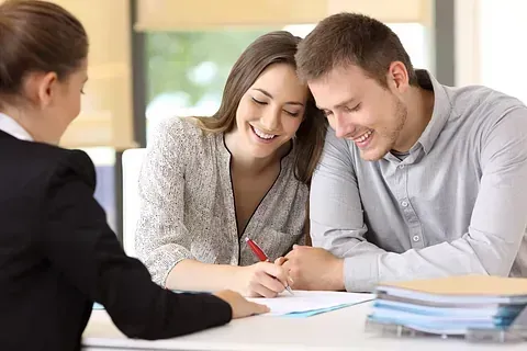 Un hombre y una mujer están sentados en una mesa firmando un documento.