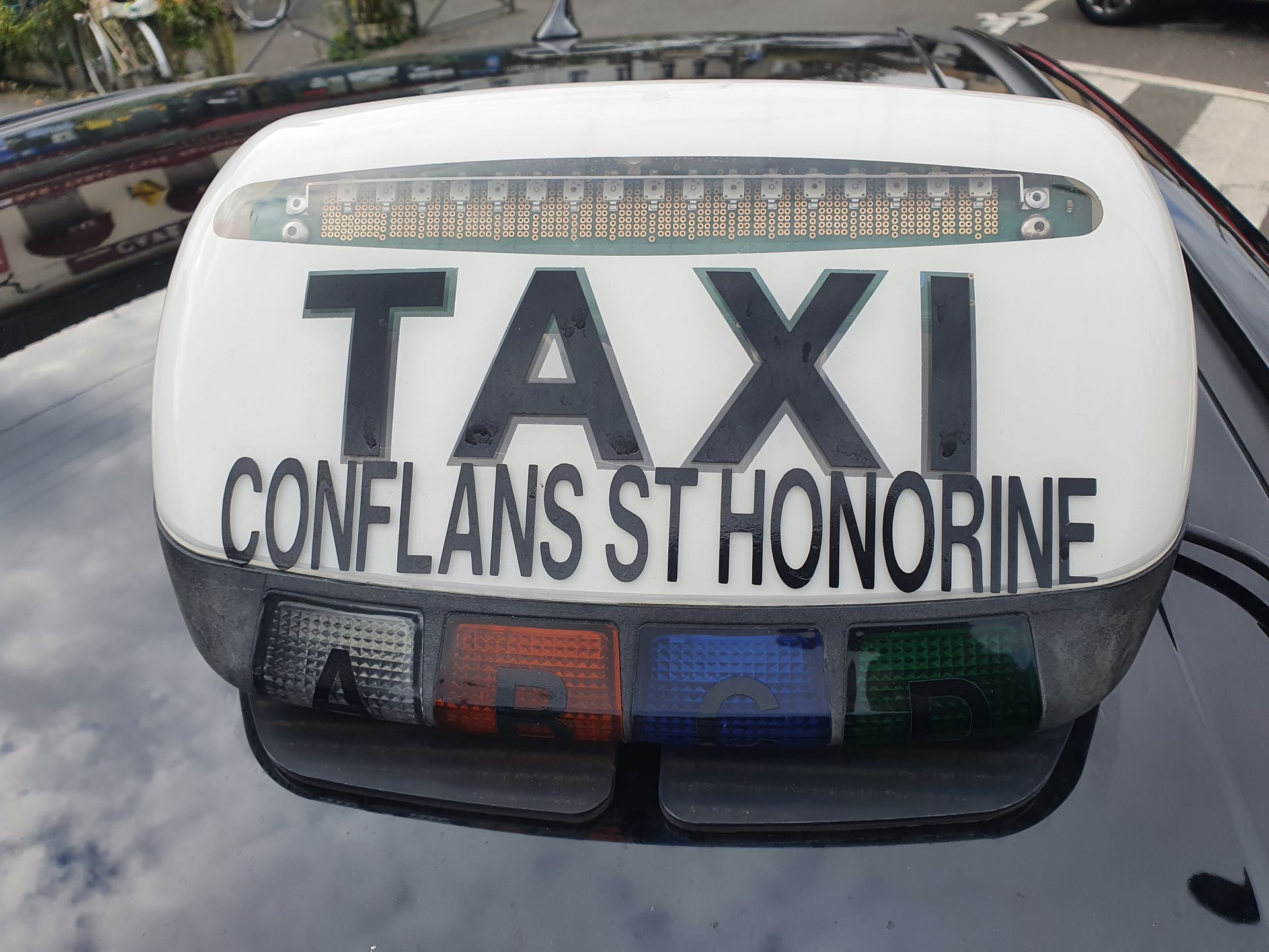 Panneau de toit de taxi à Conflans-Sainte-Honorine, France, avec TAXI illuminé et lumières colorées.