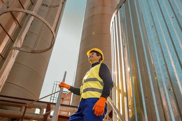 Arbeiter in Sicherheitsausrüstung blickt in der Nähe von Industrietanks nach oben.