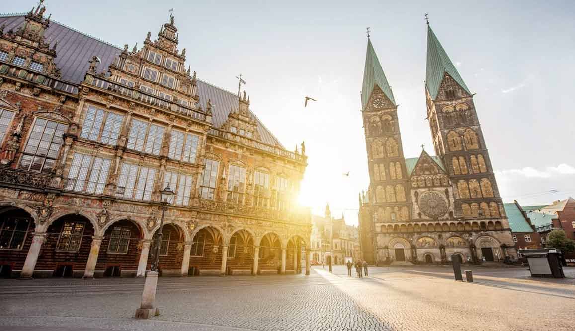 Das Bremer Rathaus und der Bremer Dom in Deutschland, in warmes Sonnenlicht getaucht, mit einem gepflasterten Platz im Vordergrund.