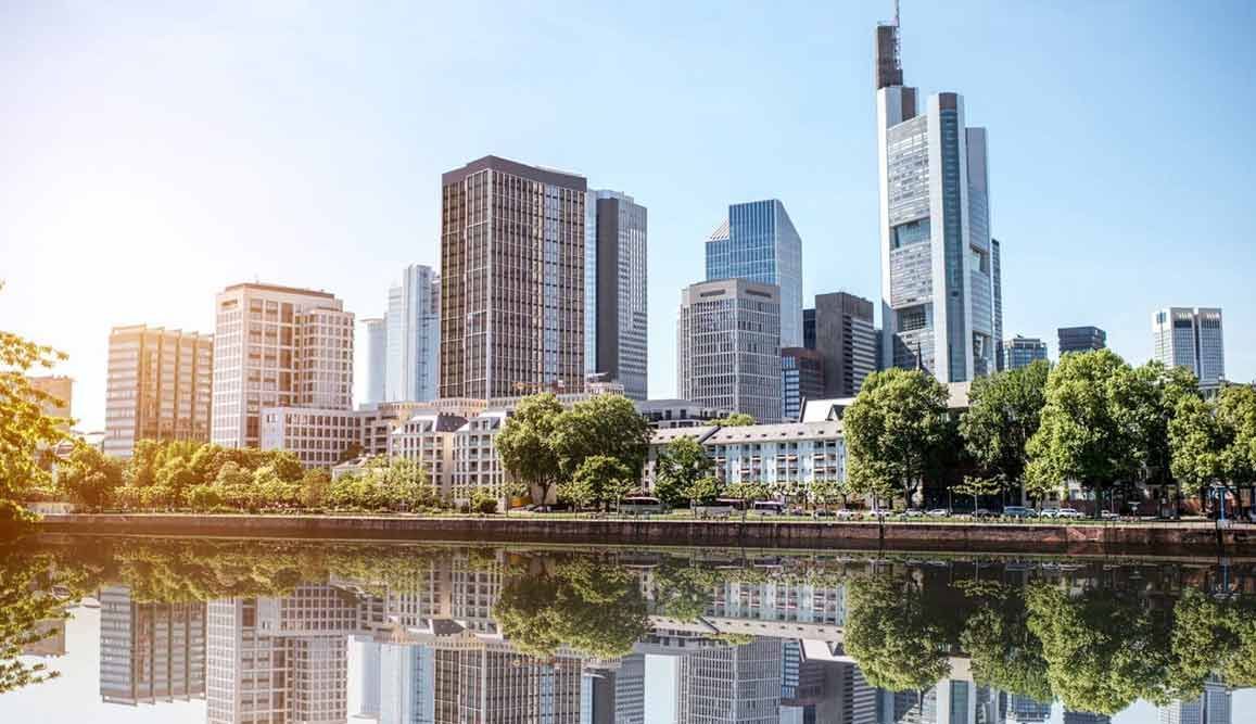 Skyline von Frankfurt, Deutschland, mit modernen Wolkenkratzern, die sich an einem sonnigen Tag in einem ruhigen Fluss spiegeln.