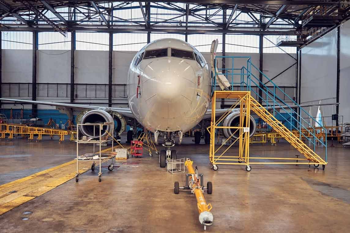 An einem weißen Passagierflugzeug wird in einem Hangar gearbeitet, mit gelbem Gerüst und Ausrüstung.