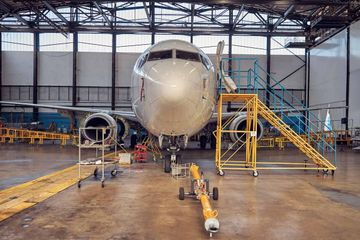 An einem weißen Passagierflugzeug wird in einem Hangar gearbeitet, mit gelbem Gerüst und Ausrüstung.