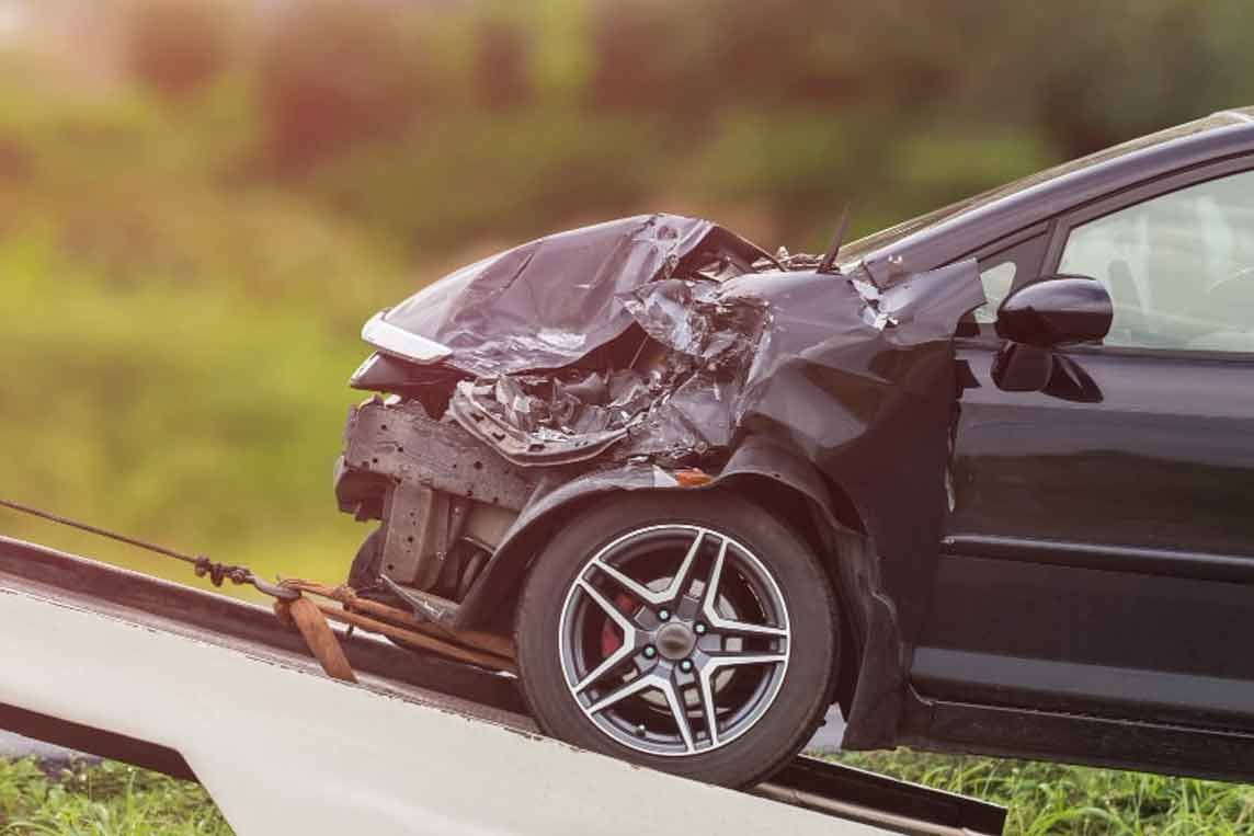 Beschädigtes schwarzes Auto nach einer Kollision auf der Rampe eines Abschleppwagens; die Frontpartie ist stark eingedrückt.