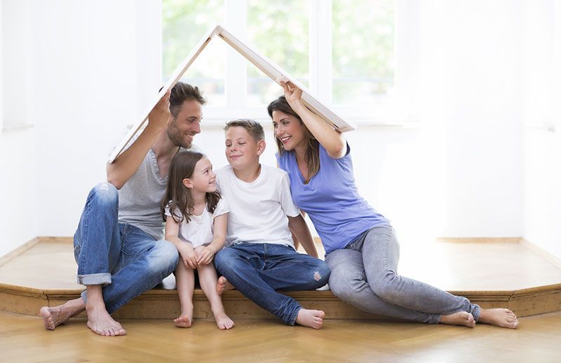 Eine Familie sitzt auf dem Boden unter einem Papphaus.