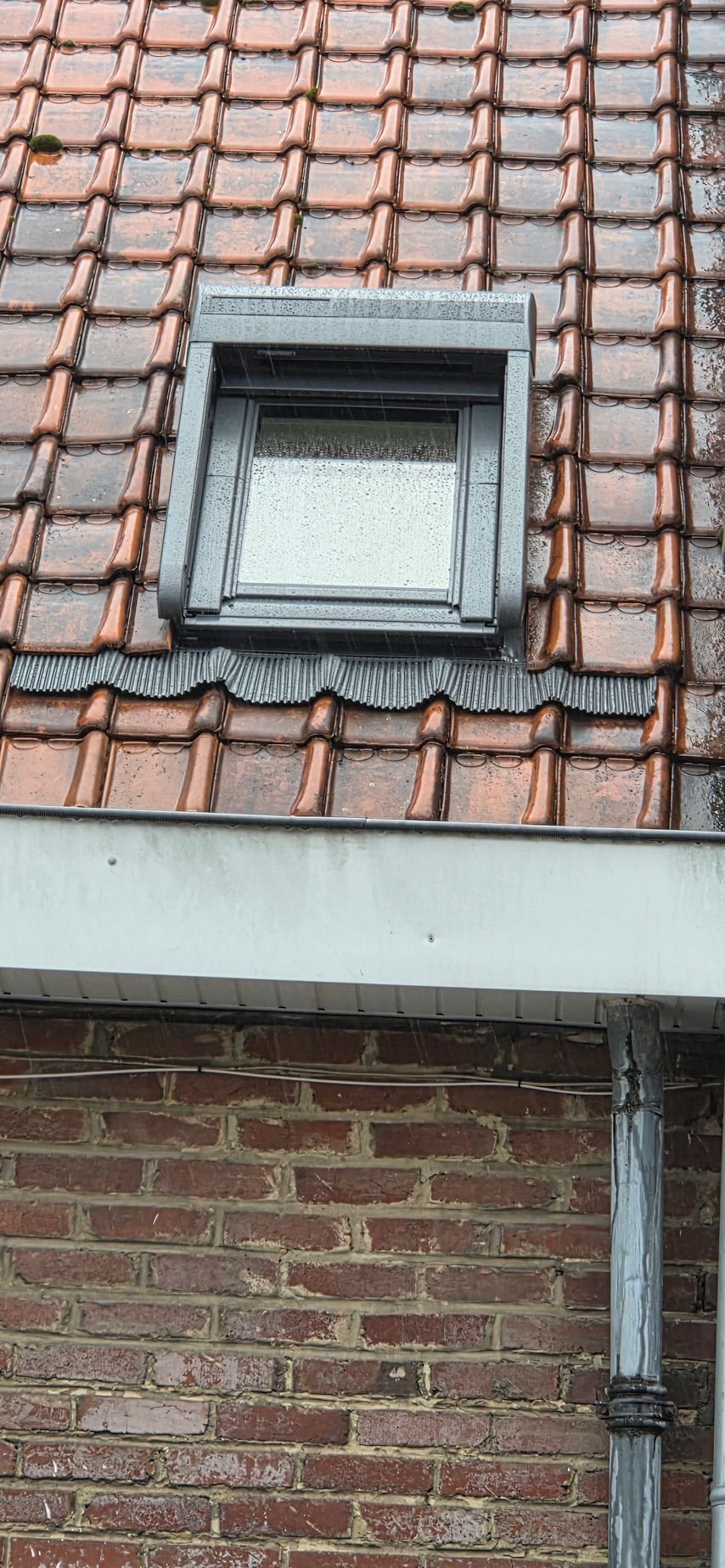 Un ouvrier portant un casque et un harnais de sécurité se penche au-dessus d'un puits de lumière sur le toit d'une maison, sur fond de ciel bleu éclatant.