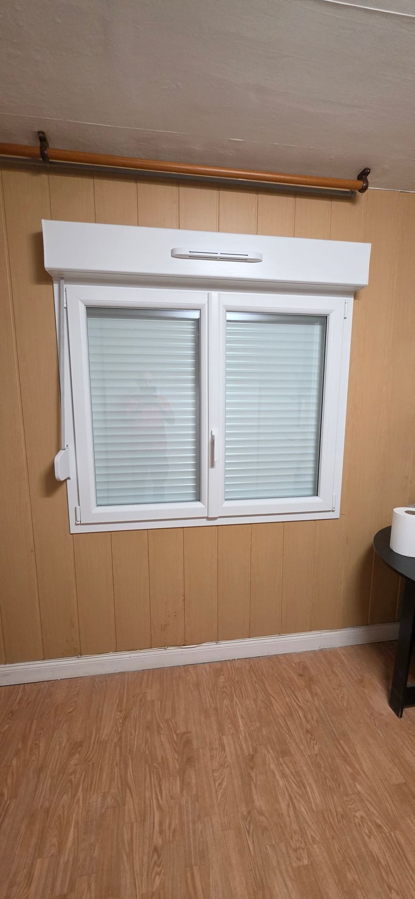 Gros plan sur un cadre de fenêtre en PVC blanc partiellement ouvert, montrant le mécanisme de verrouillage métallique sur un ciel bleu ensoleillé.