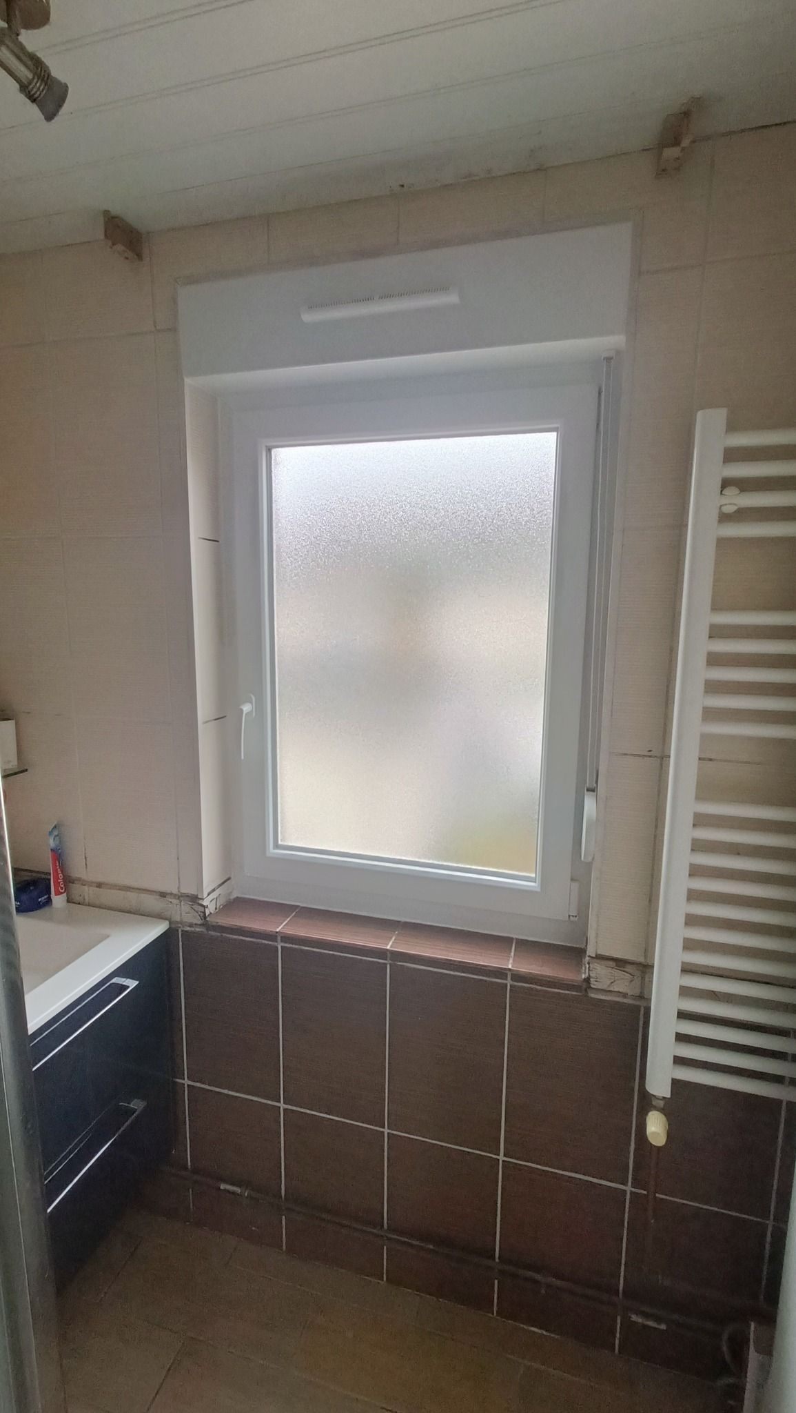 Un ouvrier ganté utilise une équerre pour mesurer le coin d'un cadre de fenêtre blanc.