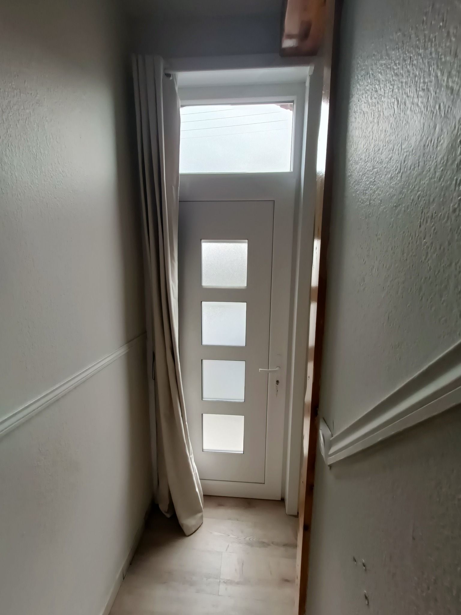 Une porte d'entrée turquoise avec un heurtoir, flanquée d'appliques murales et de plantes en pot sur un porche blanc.