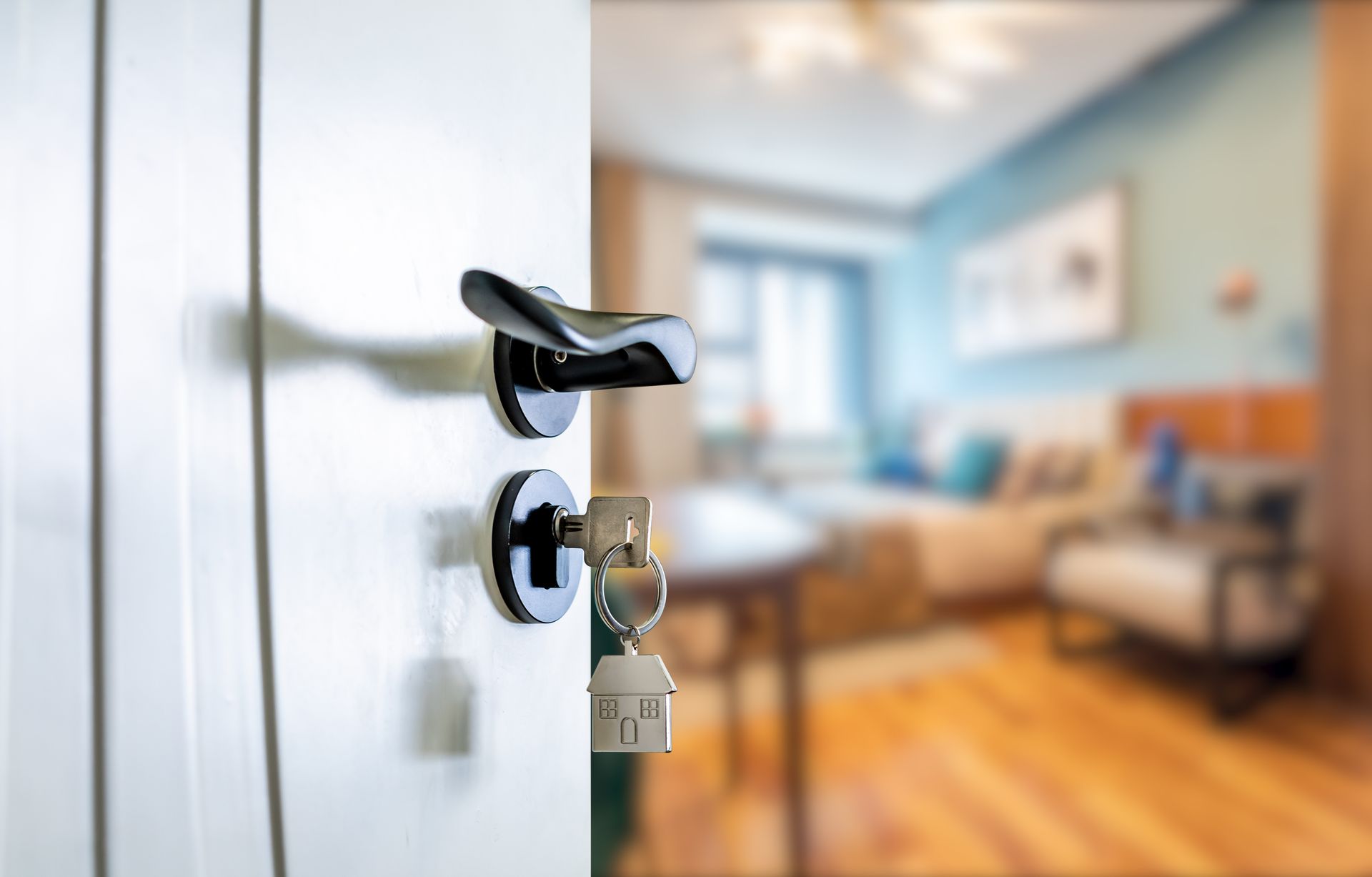 Une porte blanche entrouverte, avec un porte-clés en forme de maison accroché à la clé dans la serrure, donnant sur une pièce floue.