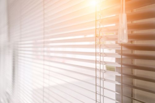 La lumière du soleil filtre à travers les stores blancs horizontaux, créant une douce lueur chaude.