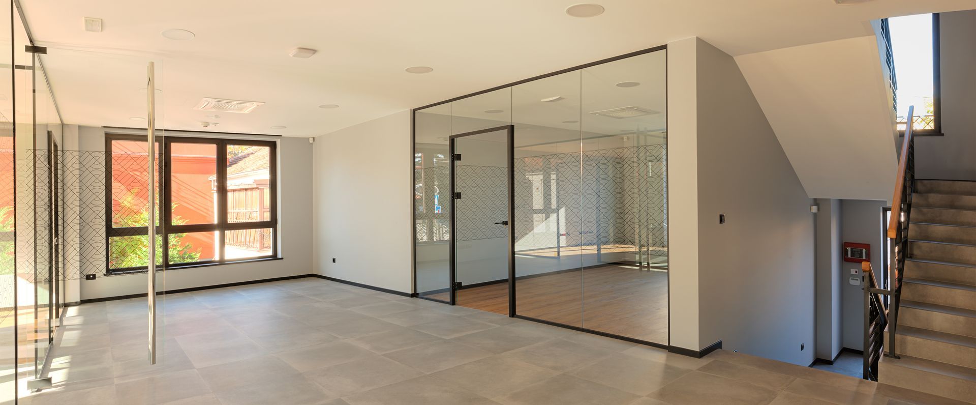 Un intérieur de bureau lumineux et moderne avec un sol carrelé clair, une salle de conférence aux parois de verre et un escalier sur la droite.