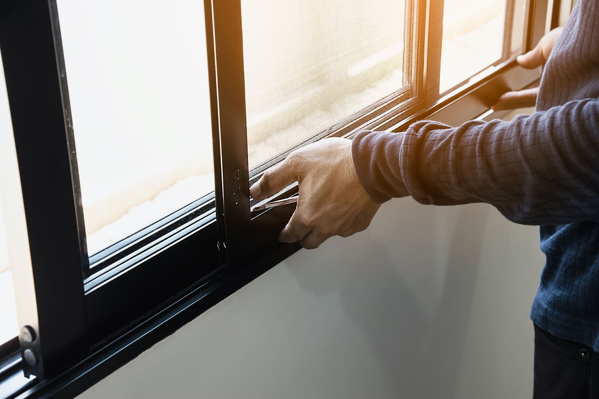 Les mains d'une personne installant ou retirant une moustiquaire noire d'un cadre de fenêtre coulissante.