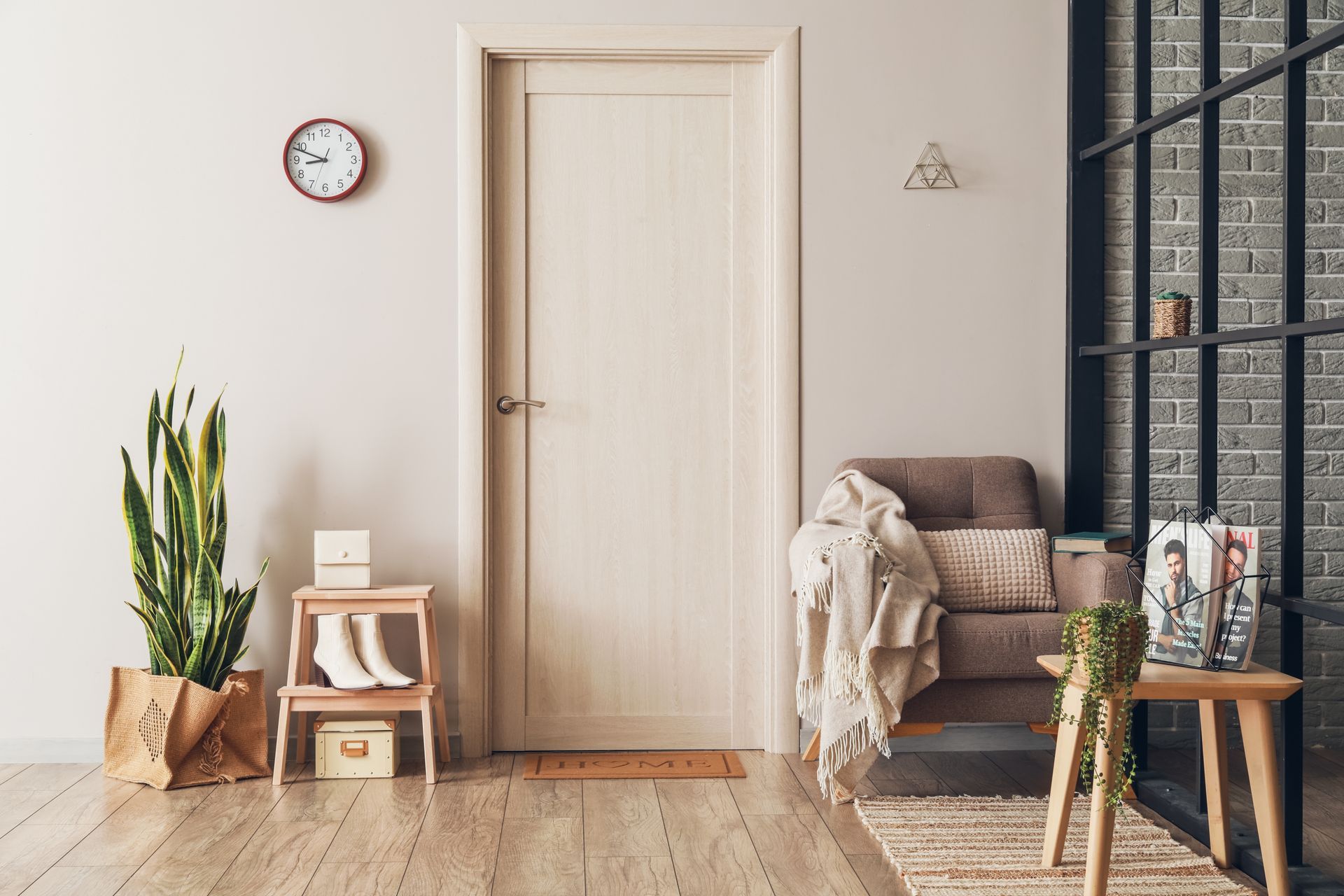 Une pièce intérieure beige avec une porte centrale, une plante serpent sur un tabouret, un petit fauteuil avec un plaid et une table d'appoint.